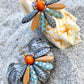 Speciel blomsterørering i blå nuancer med orange glasperle